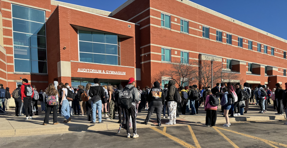 Students and staff gather outside the entrance to the auditorium after an unexpected fire alarm causes the school to be evacuated.