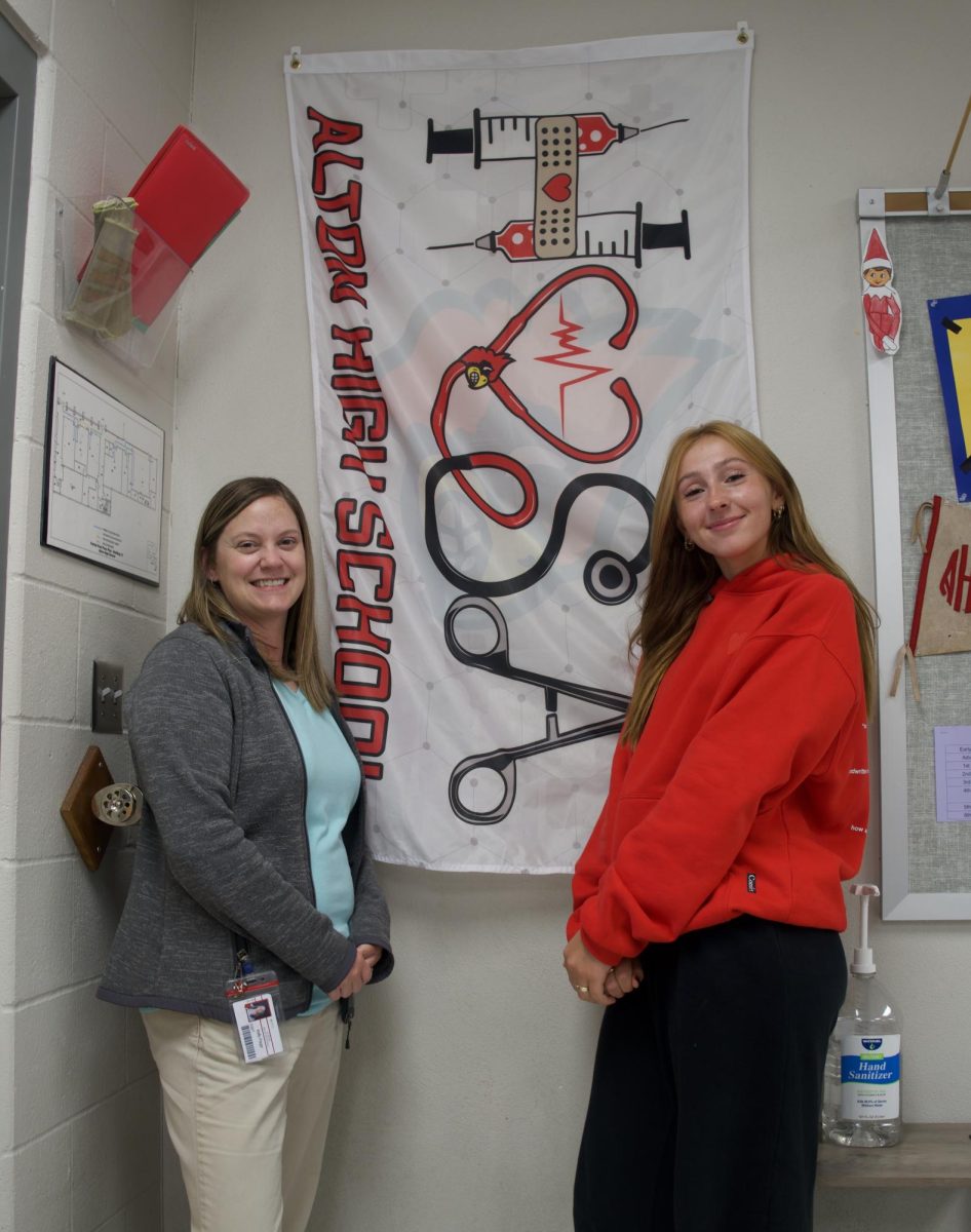 HOSA sponsor Kelly Paige and club president Katie Krafka pose in front of the HOSA flag. 
